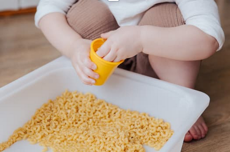 Mains d'enfants jouant dans un bac de pâtes